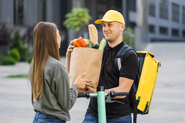 Beyaz üniformalı akıllı servis elemanı alıcıya taze yiyecek veriyor.