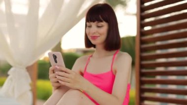 Tropik tatil beldesinde yaz tatili. Mutlu gülümseyen genç kadın, harika bir ahşap çardakta oturuyor.