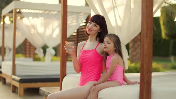 Charming young woman and her child daughter girl in pink swimsuits, hugging on the gazebo — Video