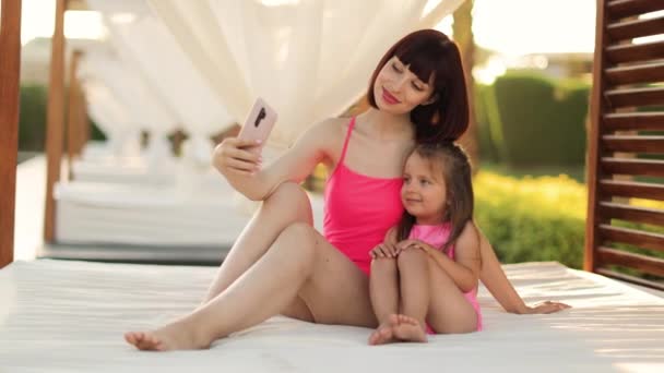 Alegre joven madre y su pequeña hija linda en el mismo traje de baño rosa sentado en gazebo — Vídeos de Stock