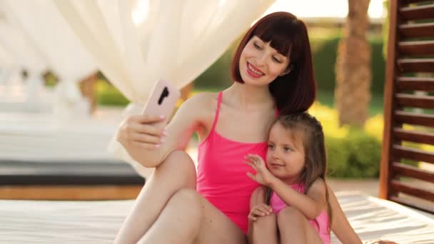 Joyful jovem mãe e sua filhinha fofa nos mesmos trajes de banho rosa sentado no gazebo — Vídeo de Stock