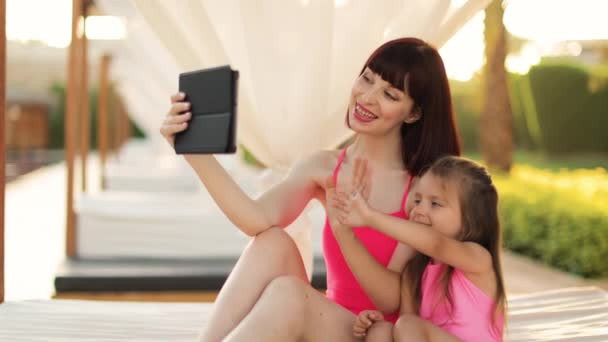 Szczęśliwa uśmiechnięta mama trzyma tablet ze swoją córeczką podczas odpoczynku w altanie na świeżym powietrzu — Wideo stockowe
