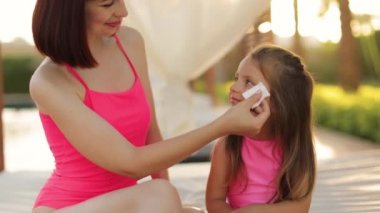 Genç, sevecen, beyaz bir anne, pembe mayo giyiyor, havuz kenarındaki tahta bir çardakta oturuyor.