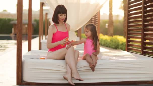 Young pretty woman applying sunscreen spray on hand of her daughter in a pink swimsuits — Stock Video