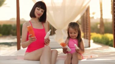 Güzel bir anne kızıyla birlikte yüzme havuzunun yanında bir çardakta oturuyor.