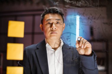 Asyalı işadamı turuncu notlarla cam tahtaya pasta grafiği çiziyor