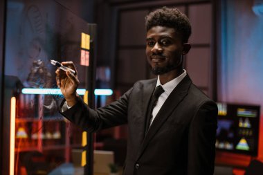 Afrikalı Amerikalı ofis çalışanı cam levhalara görev ya da fikirler yazıyor.