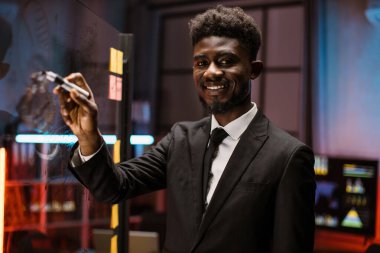 Afrikalı Amerikalı ofis çalışanı cam levhalara görev ya da fikirler yazıyor.