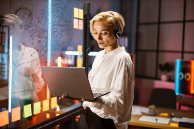 Kafkasyalı iş kadını, video görüşmesi için dizüstü bilgisayar kullanıyor, cam tahtanın yanında duruyor.