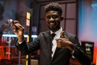 Afrikalı Amerikalı ofis çalışanı cam levhalara görev ya da fikirler yazıyor.