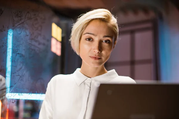 Femme d'affaires caucasienne en chemise blanche, posant sur la caméra, tout en se tenant dans le bureau sombre moderne — Photo