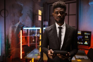 Elinde tabletle karanlık ofiste yapışkan notlar tutan Afro-Amerikan bir adam.