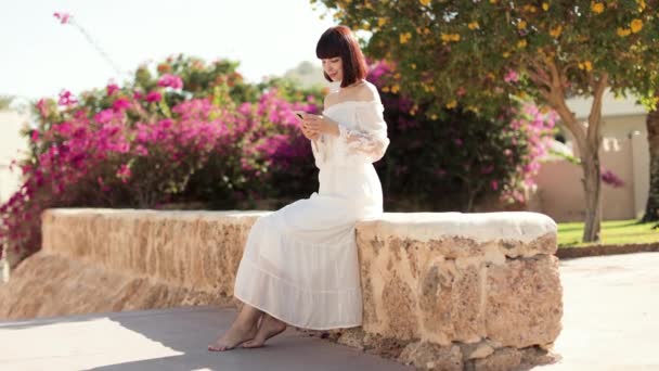 Fericit călător caucazian femeie în rochie albă folosind telefonul mobil la oraș tropical. — Videoclip de stoc