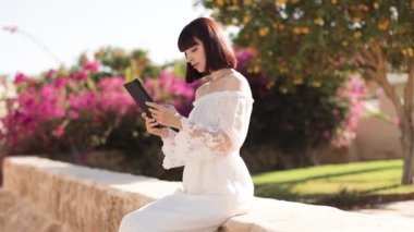 Yaz tatilinde tropikal bir tatil köyünün yanında otururken tablet kullanan güzel bir kız..