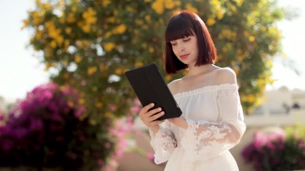 Mujer viajera feliz en vestido blanco y sombrero de paja usando tableta leyendo noticias en Internet — Vídeo de stock