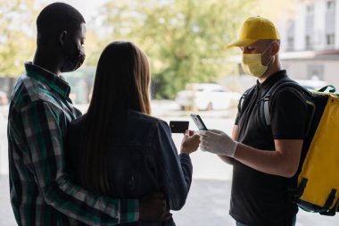 Beyaz maskeli bir adam pizza ya da fast food servisi yapıyor..