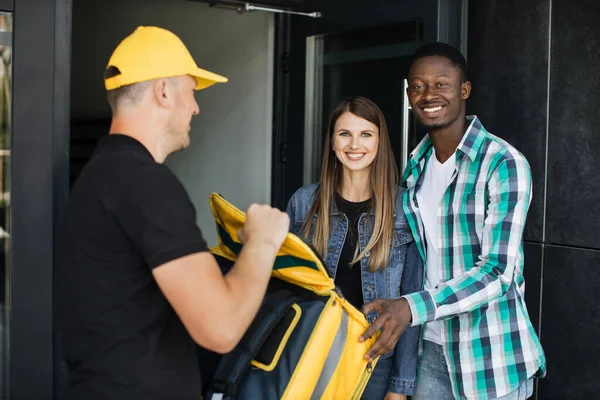 Courier delivering parcel for multinational couple at the door of their house. — Foto de Stock