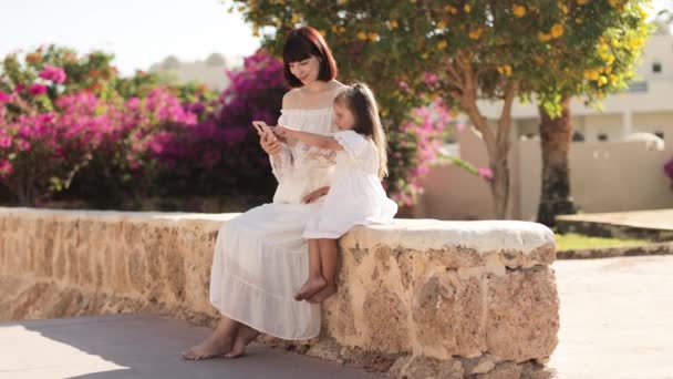 Attractive young woman tourist and her little cute daughter speaking using smartphone — Vídeos de Stock