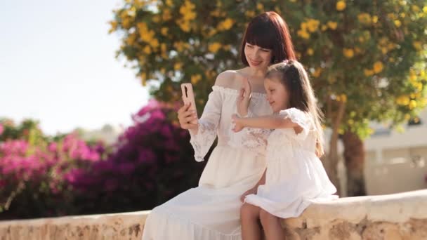 Mother and daughter taking selfie on smartphone while sitting on background on tropical view — 비디오