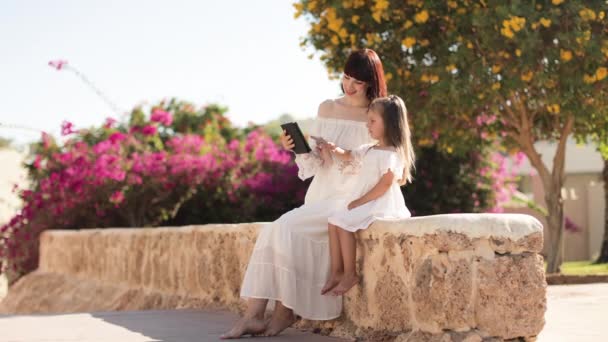 Happy modern mother and daughter in white dresses and straw hats near the hotel — Vídeos de Stock