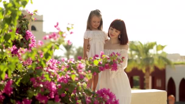 Retrato de cerca de la joven madre y su pequeña niña pasando tiempo cerca del árbol floreciente. — Vídeo de stock