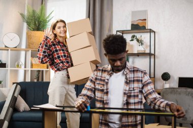 Kadın kutuları tutarken, erkek yeni evdeki rafları ölçüyor.