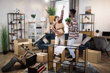 Multiracial couple dancing at living room with boxes around