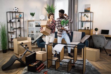 Oturma odasında kutularla dans eden çok ırklı bir çift.