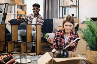 Diverse family assembling shelf and unpacking boxes at home
