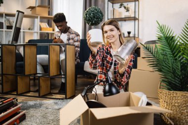 Wife unpacking boxes while husband assembling shelves