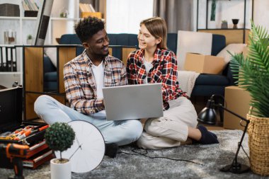 Yeni dairede dizüstü bilgisayar kullanan neşeli, çok kültürlü bir aile.