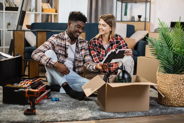 Genç çok ırklı aile evde karton kutuları açıyor.