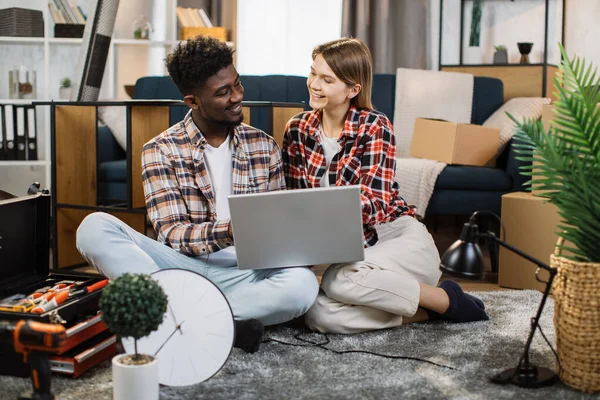 Yeni dairede dizüstü bilgisayar kullanan neşeli, çok kültürlü bir aile.