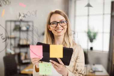 Tabletle cam tahtanın yanında duran kadın ofis çalışanı.