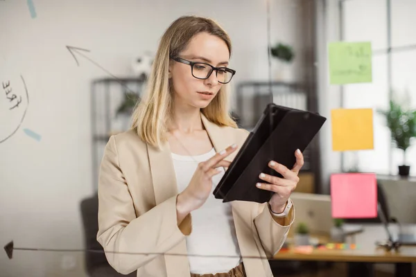 Femme confiante en costume en utilisant une tablette près du panneau de bureau en verre — Photo