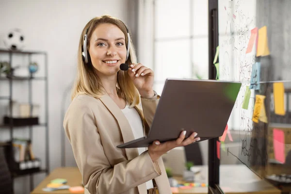 Heureuse femme d'affaires dans casque tenant ordinateur portable à la salle de bureau — Photo