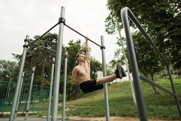 근육질 몸통을 가진 젊은 코카서스 운동 선수가 크로스바에서 모퉁이를 돌고 있다 — 스톡 사진