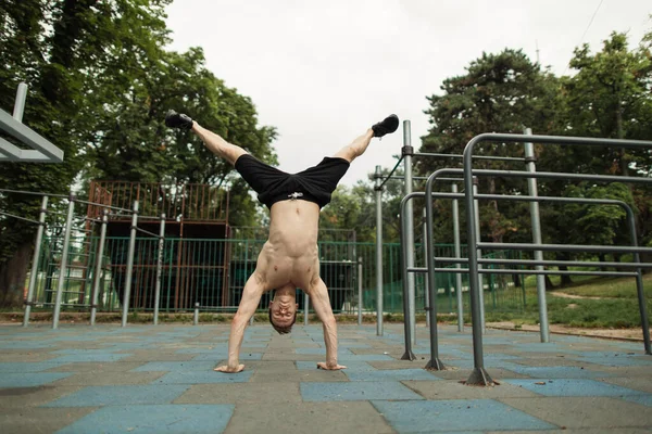 Shirless man doet een handstand op de outdoor gym. — Stockfoto