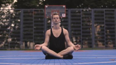 Açık spor salonunda yoga yapan, siyah spor kıyafetli, beyaz bir genç. Çekici adam sabah vakti Lotus pozisyonunda oturuyor..