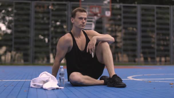 Sportowy Mięśniak Siedzący Podłodze Boiska Koszykówki Odpoczywający Przed Porannym Bieganiem — Wideo stockowe