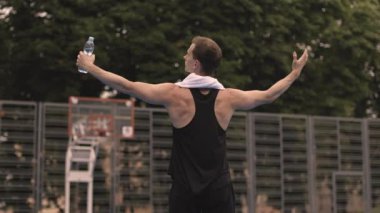 Spor elbiseli kaslı bir gencin, açık şehir spor salonunda elleri kenarda duruşu. Beyaz erkek sporcu dışarıda antrenman yaparken dinleniyor..