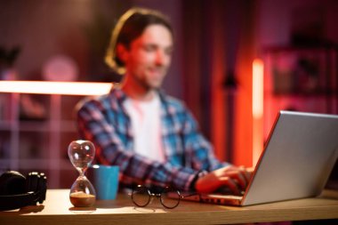 Evde akşamları modern dizüstü bilgisayarda çalışan odaklanmış beyaz bir adam. Mavi kareli gömlek giyen genç bir hippi. İnsan kavramı, serbest çalışma ve teslim tarihi.