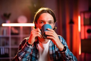 Ofiste kahve, çay ya da sıcak içecek içen kendinden emin genç bir adam. Akşamları modern ofiste ya da evde çalışan beyaz erkek işçi..