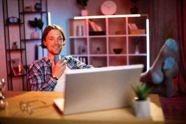 Çekici genç adam elinde bir kupa sıcak içecekle masada oturuyor ve bilgisayar ekranına bakıyor. Gündelik giysiler içindeki neşeli kadın, çalışma saatleri boyunca evde mola veriyor..