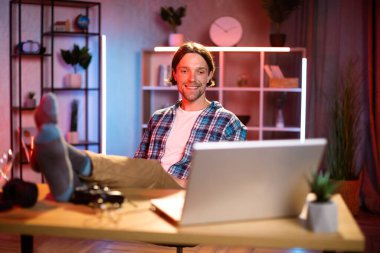 Çekici genç adam elinde bir kupa sıcak içecekle masada oturuyor ve bilgisayar ekranına bakıyor. Gündelik giysiler içindeki neşeli kadın, çalışma saatleri boyunca evde mola veriyor..