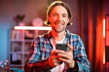 Akşamları evde akıllı telefon kullanan kareli gömlekli beyaz bir adamın portresi. Modern aletlerle yaşam tarzları.