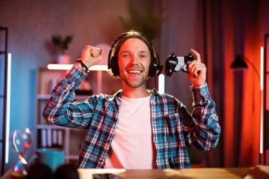 Video oyunlarında zaferi kutlarken kulaklıklı, bağıran ve el kol hareketi yapan neşeli genç bir adam. Boş zamanlarında kulaklık ve joystick kullanan çekici bir adam..