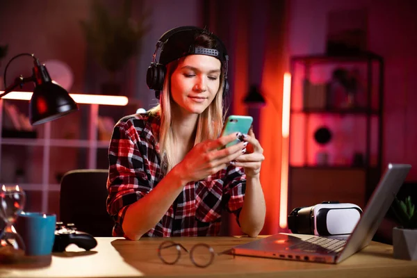 Sevimli bir kadın en sevdiği şarkıyı dinlemek için akıllı telefon ve kulaklık kullanıyor. Evde dizüstü bilgisayarla uğraşırken şapkalı genç bayan mola veriyor. Serbest ve teknoloji kavramı.