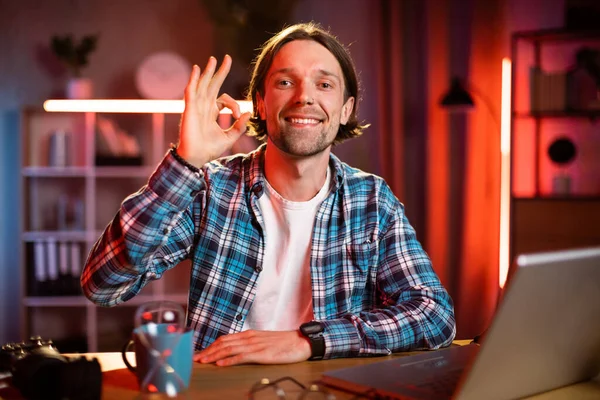 Çekici bir adam masada oturuyor, elleri göğsünde çaprazlanmış ve kameraya bakıyor. Gündelik giysiler içindeki beyaz erkek çalışma saatleri boyunca evde mola veriyor..