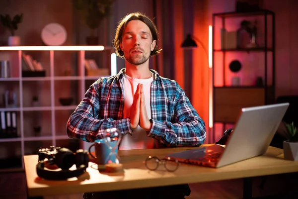 Kareli gömlekli gülümseyen beyaz adamın portresi. Akşam evde yoga egzersizi yapıyor. Uzaktan kumanda sırasında meditasyon için ara veren mutlu genç adam..